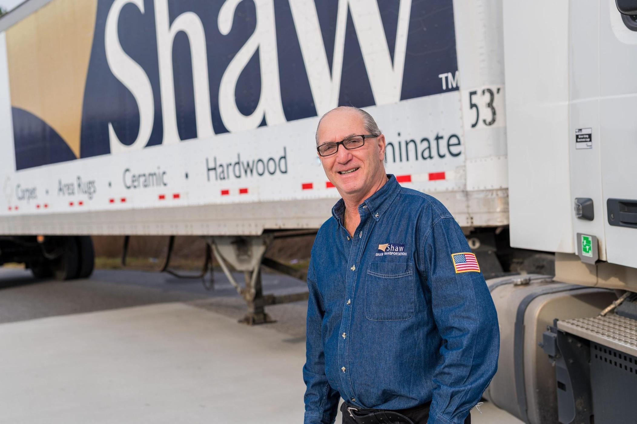 Male truck driver standing on the side of a Shaw semi truck